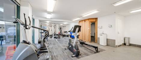 A modern gym with various exercise equipment, a large mirror, and a view of the outside through glass doors.