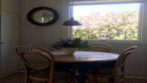 A dining table with four wicker chairs, a vase with purple flowers, a wall-mounted mirror, and a window with a view of pink trees. - 4 Star Holiday Home in Nykobing Sj (Nykobing Sjaelland)