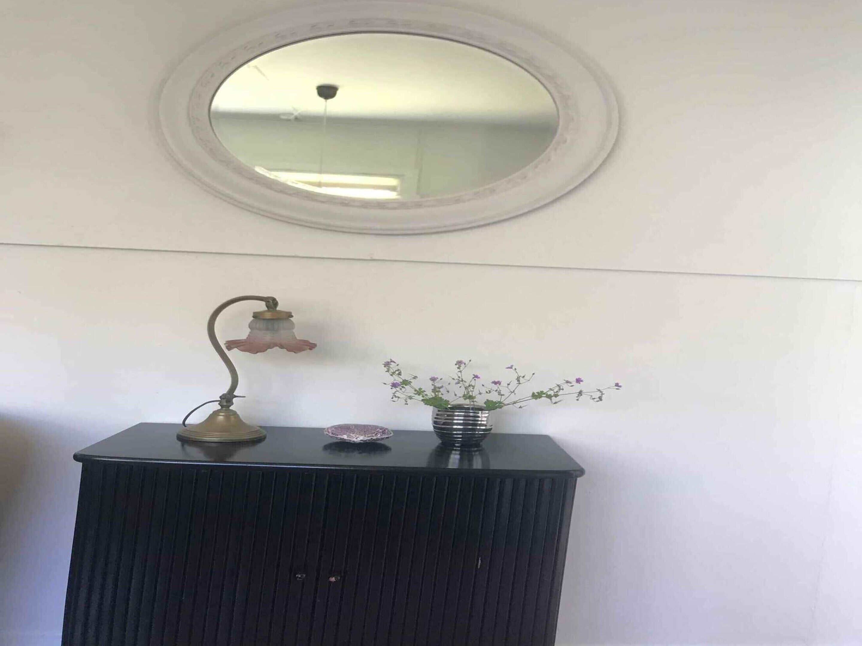 Un tocador de baño con espejo redondo, una lámpara de pared y un florero con flores.