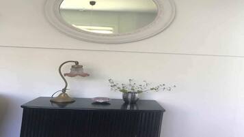 Un tocador de baño con espejo redondo, una lámpara de pared y un florero con flores.
