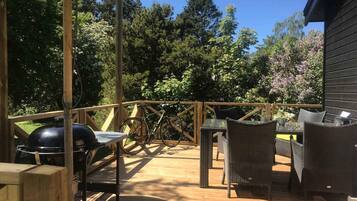Una terraza de madera con mobiliario exterior, una parrilla y una bicicleta.
