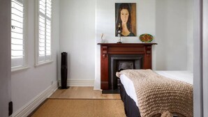 A bedroom with a bed, a fireplace, a painting, and a window with blinds. - Elegant 3-bed Heritage House With Swimming Pool (Sydney)