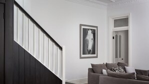 A modern living room with a dark wooden staircase, a grey sofa set, and a framed horse portrait on the wall. - Elegant 3-bed Heritage House With Swimming Pool (Sydney)