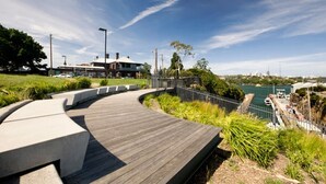 A curved wooden deck with a railing, overlooking a body of water and a cityscape. - Elegant 3-bed Heritage House With Swimming Pool (Sydney)
