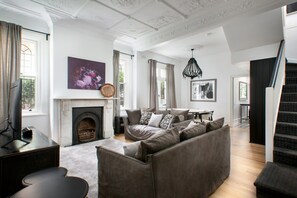 A spacious living room with a fireplace, a sofa set, and a staircase. - Elegant 3-bed Heritage House With Swimming Pool (Sydney)