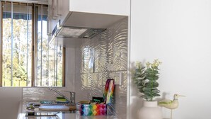 A modern kitchen with a large window, a colorful storage unit, and a decorative bird sculpture. - Seafront Getaway Studio, Great Location With Pool (Batehaven)