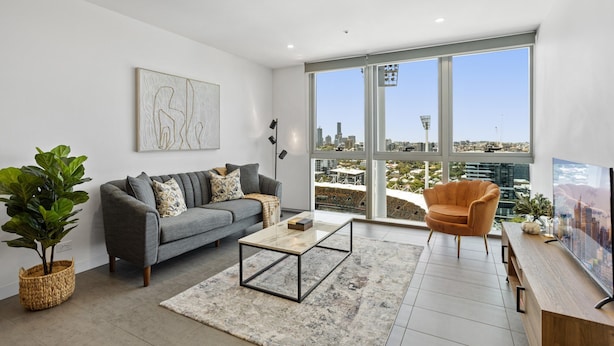 Un salón moderno con un sofá gris, una mesa de centro y un ventanal con vistas a la ciudad.