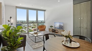 Una sala de estar moderna con comedor, ventanas amplias, televisor y vista de la ciudad.