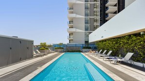 Una piscina en la azotea con sillones de descanso y un edificio moderno al fondo.