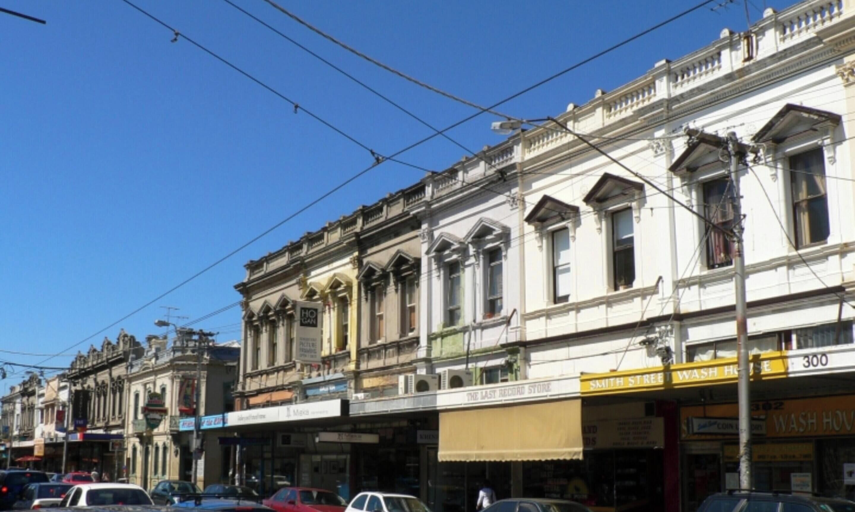 Una calle con edificios históricos, una tienda de discos y un local amarillo con un letrero que dice 'WASH HOUSE'.
