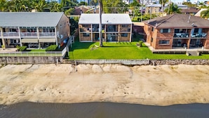 Une propriété située en bord de mer, comprenant un bâtiment à deux étages, une pelouse bien entretenue et une plage de sable.