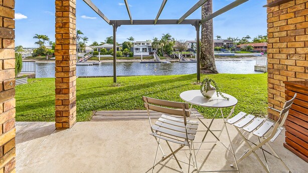 Une terrasse avec une table et des chaises donnant sur un plan d’eau et des immeubles résidentiels.