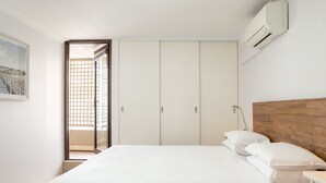Une chambre à coucher comprenant un lit, une tête de lit en bois, une armoire et une porte donnant sur un balcon.