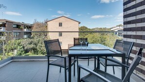 A balcony with a glass table and chairs, two wine glasses, and a view of a brick building and trees. - Professional Living Minutes From the City (Sydney)