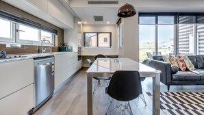 A modern kitchen with a dishwasher, a dining table with chairs, and a black leather sofa with cushions. - Professional Living Minutes From the City (Sydney)