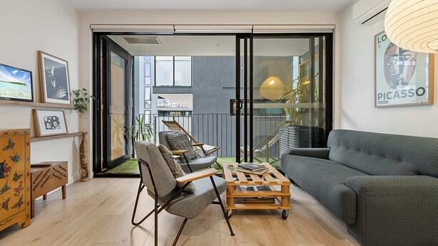 A modern living room with a sofa, chairs, and a coffee table. There is a sliding glass door leading to a balcony with plants. - City View Haven in South Melbourne (Melbourne)