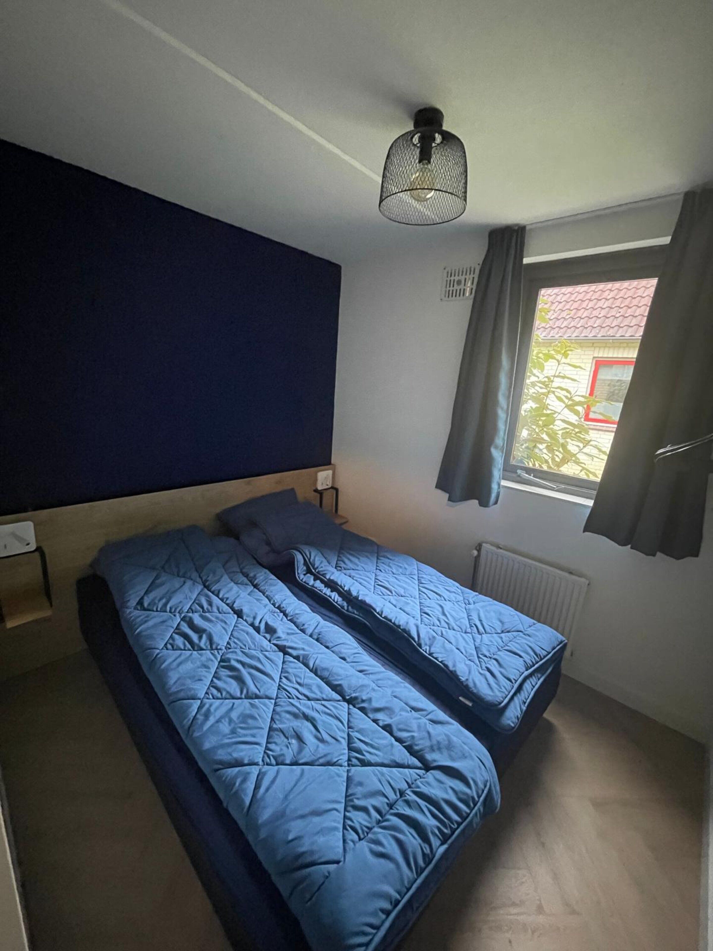 A room with a bed, a window with curtains, a radiator, and a ceiling light fixture.