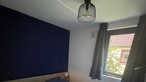 A room with a bed, a window with curtains, a radiator, and a ceiling light fixture. - Sunny Family Bungalow by the Lake (Ewijk)
