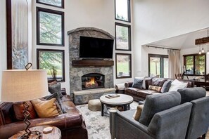 A spacious living room with a stone fireplace, leather sofas, and a large TV. - 4BR Mountain Home | Fireplace & Pool + Shuttle (Edwards)