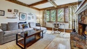 Ein gemütliches Wohnzimmer mit Holzboden, Kamin, einer Couch, einem Couchtisch und einem Schreibtisch mit Stuhl.