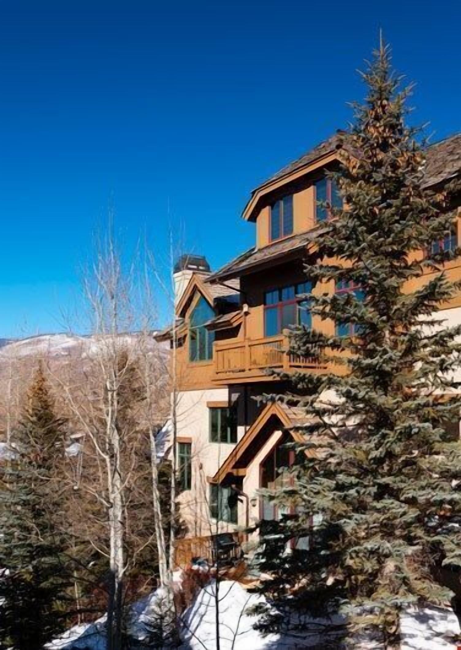 Un chalet à étages, doté d’une façade en bois, de grandes fenêtres et d’un balcon.