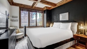 Ein Schlafzimmer mit einem großen Bett, einem Schreibtisch und einem Stuhl. Es gibt Fenster mit Jalousien, eine Heizung und Kunstwerke an den Wänden.