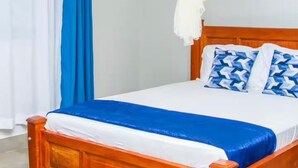 Uma cama de madeira com dossel branco, cortinas azuis e almofadas estampadas.