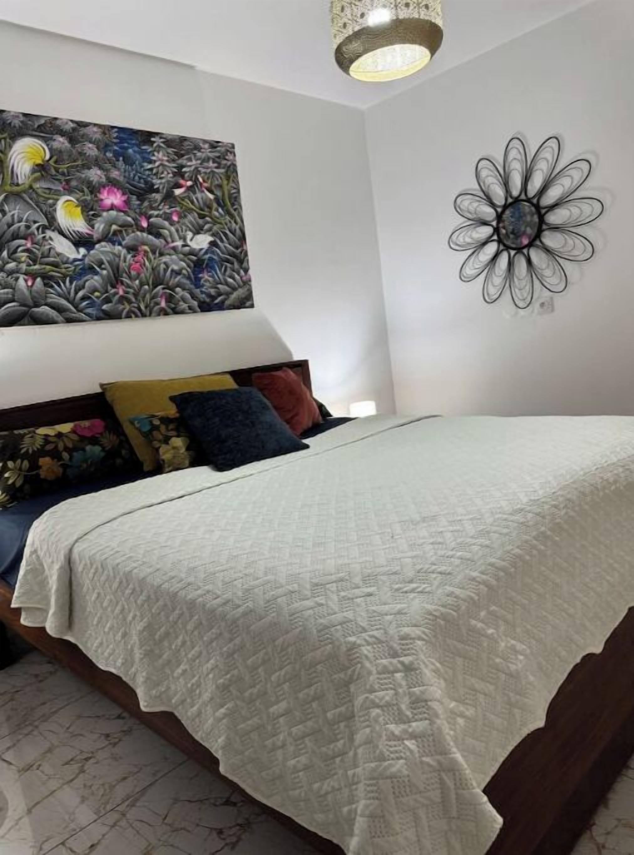 A bedroom with a bed, a decorative wall piece, and a large floral painting.