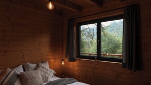 A wooden cabin room with a bed, pillows, a blanket, and a window with curtains. - Chata Cedrus (Hradištko)