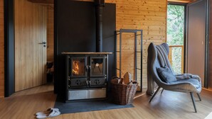 A cozy room with a wood-burning stove, a comfortable chair, and a basket of firewood. - Chata Cedrus (Hradištko)