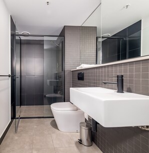 A modern bathroom with a glass-enclosed shower, a white toilet, and a large sink with a mirror above it.