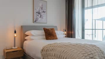 A neatly made bed with a brown pillow, a white throw blanket, and a bedside table with a lamp and a small box.