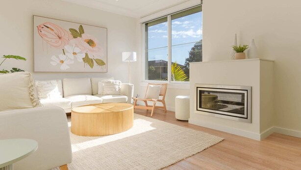 A modern living room with a white sofa, a round wooden coffee table, a white armchair, a large window with a view, and a fireplace. - Idyllic 4-bed Home With Alfresco Area Near Beach (Sydney)