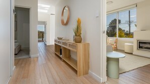 A modern interior with a wooden console table, a round mirror, and a seating area with a small round table and chairs. - Idyllic 4-bed Home With Alfresco Area Near Beach (Sydney)