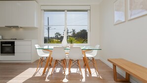 A modern kitchen with white cabinets, a glass dining table, and white chairs. - Idyllic 4-bed Home With Alfresco Area Near Beach (Sydney)