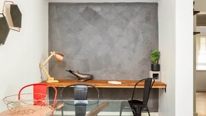 A modern office space with a large grey textured wall, a wooden desk, a red chair, a black chair, a glass table, a lamp, a fish sculpture, and a potted plant. - Suburban Two-bed Apartment With Parking and Patio (Sydney)
