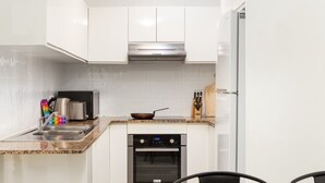 A compact kitchen with white cabinets, a stainless steel range hood, a built-in oven, and a microwave. - Suburban Two-bed Apartment With Parking and Patio (Sydney)