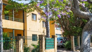 A building with a yellow facade, a green fence, and a tree with purple flowers. - Suburban Two-bed Apartment With Parking and Patio (Sydney)