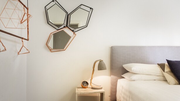 A bedroom with a bed, bedside table, lamp, and three wall-mounted mirrors. - Suburban Two-bed Apartment With Parking and Patio (Sydney)