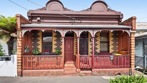 A two-story brick building with a red front door, a balcony with a metal railing, and a decorative cornice.