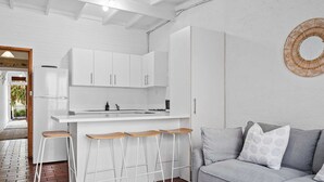 A modern kitchen with white cabinets, a central island with stools, and a grey sofa in a living area.