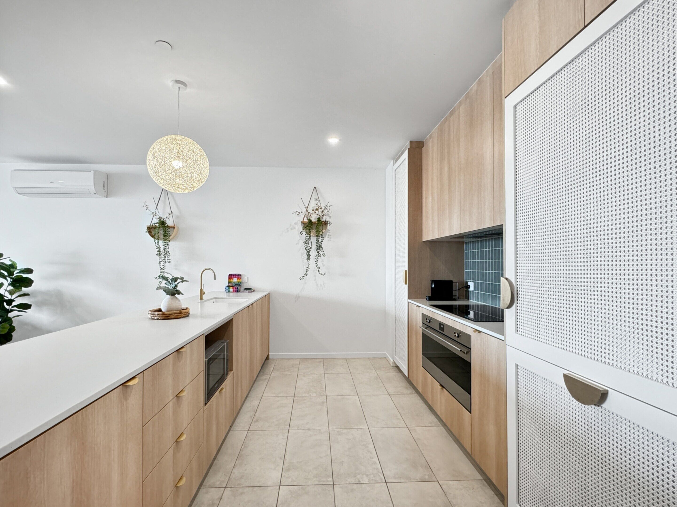 A modern kitchen with wooden cabinets, a white countertop, a hanging light fixture, and two wall-mounted planters.