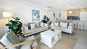 Una sala moderna con dos sofás, una mesa de centro y un sillón. Hay una zona de cocina con barra y taburetes.