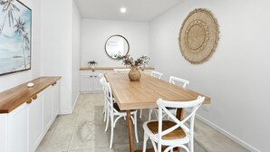 Un comedor con mesa de madera y sillas blancas, una pequeña isla con una planta, y un espejo montado en la pared.
