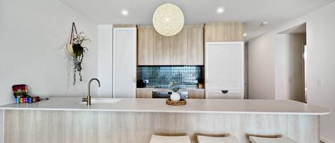 Una cocina moderna con una isla grande, taburetes blancos de bar y una lámpara colgante.