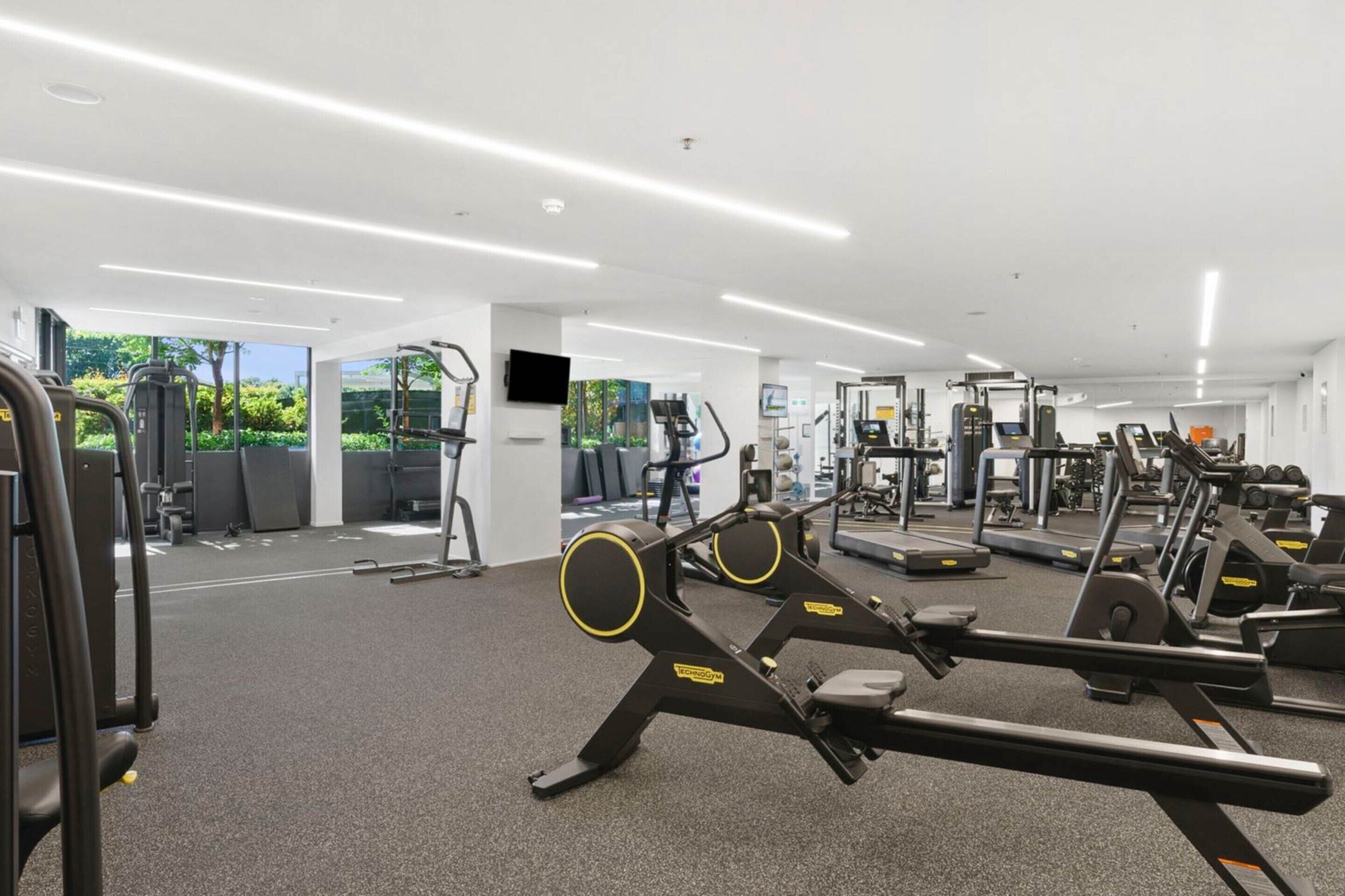 A modern gym with various exercise equipment, large windows, and a clean, well-lit interior.