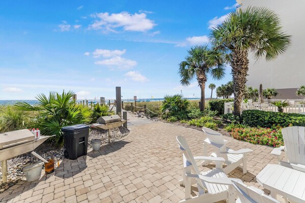 A patio area with outdoor seating, a grill, and a view of the beach.