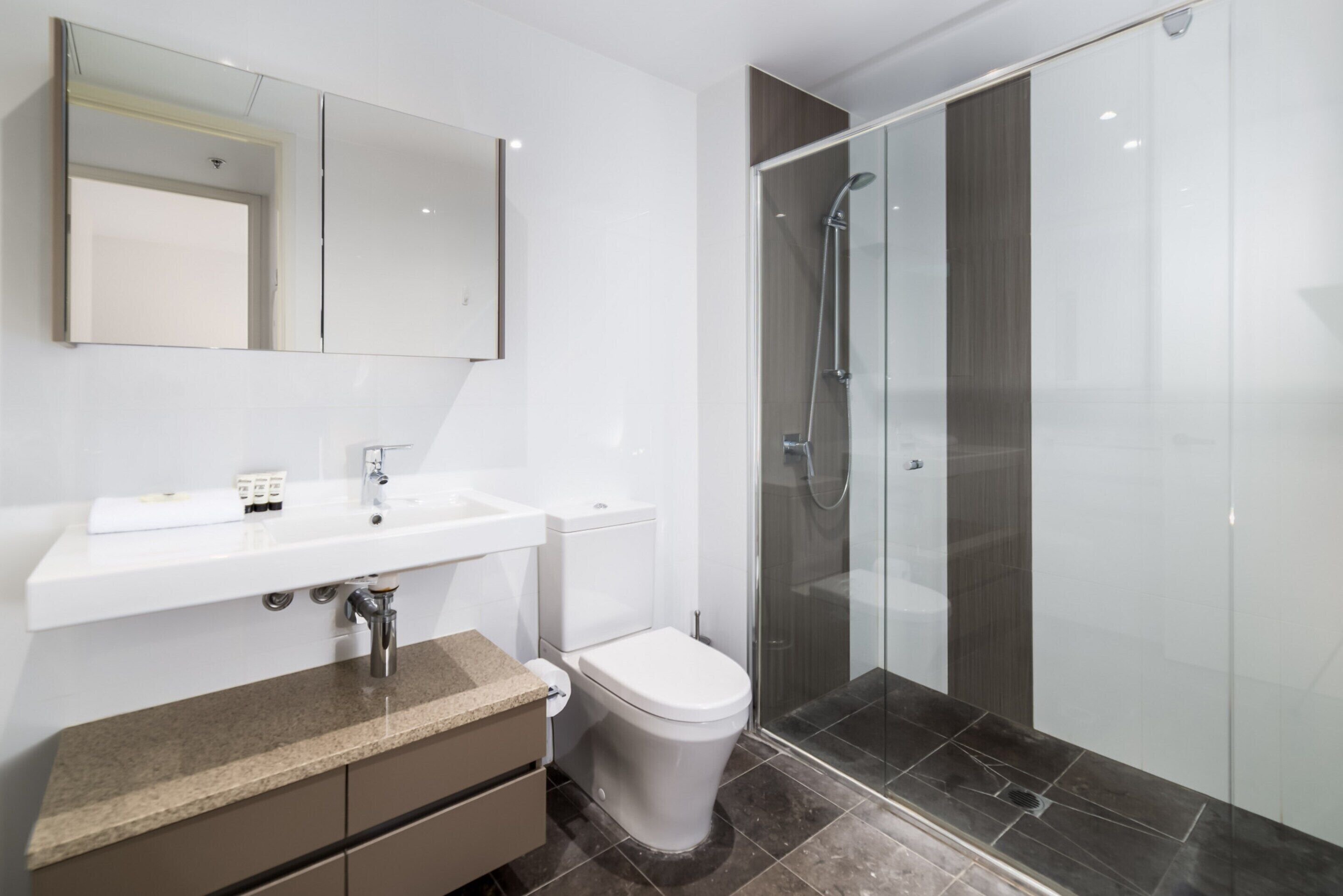 A modern bathroom with a white sink, a toilet, and a glass-enclosed shower.