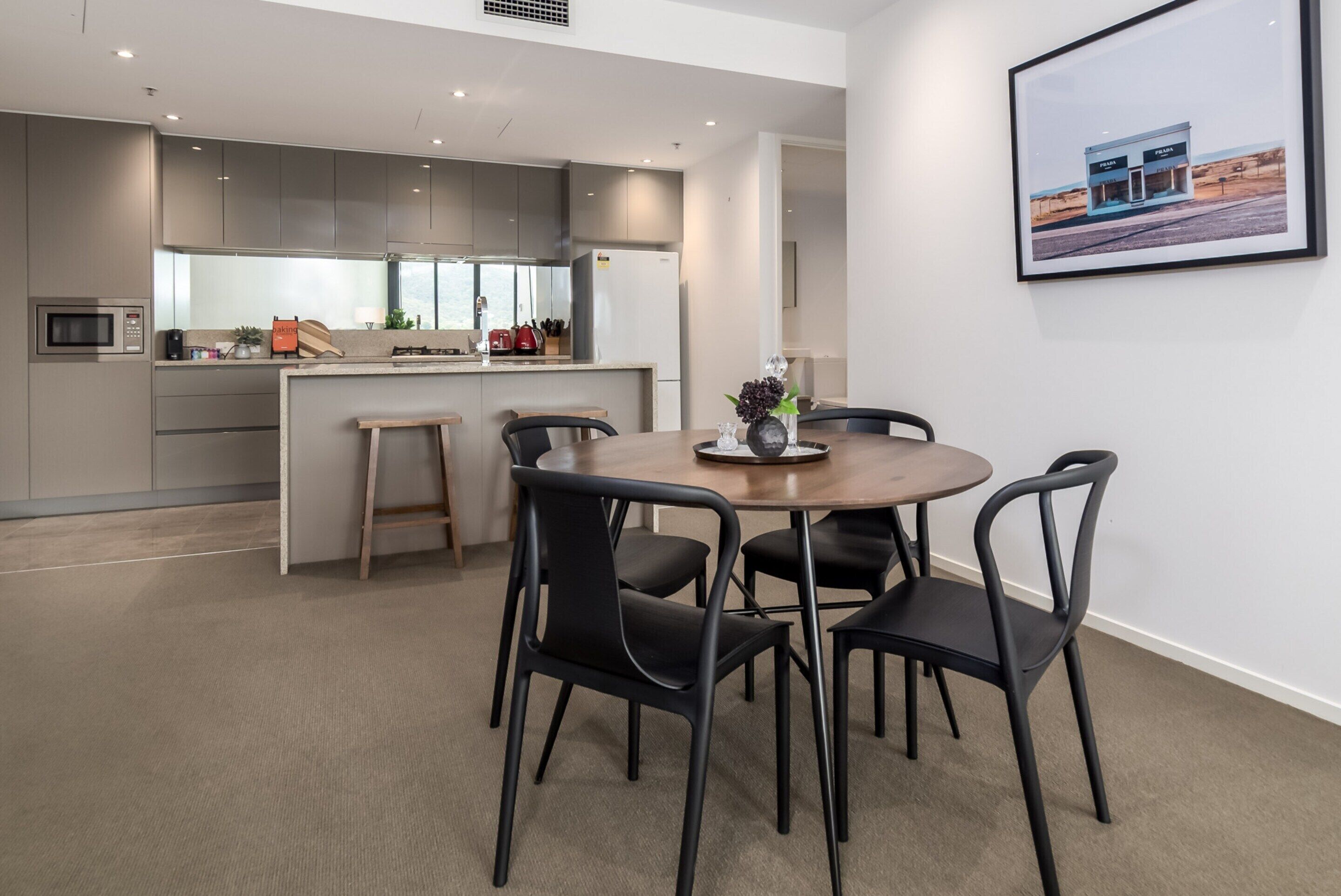 A modern kitchen with grey cabinets, a central island, and a dining area with a round table and black chairs.