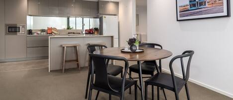 A modern kitchen with grey cabinets, a central island, and a dining area with a round table and black chairs.
